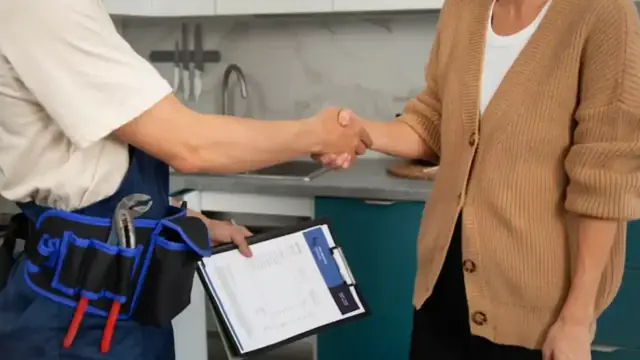 A plumber with a clipboard shaking hands with a homeowner