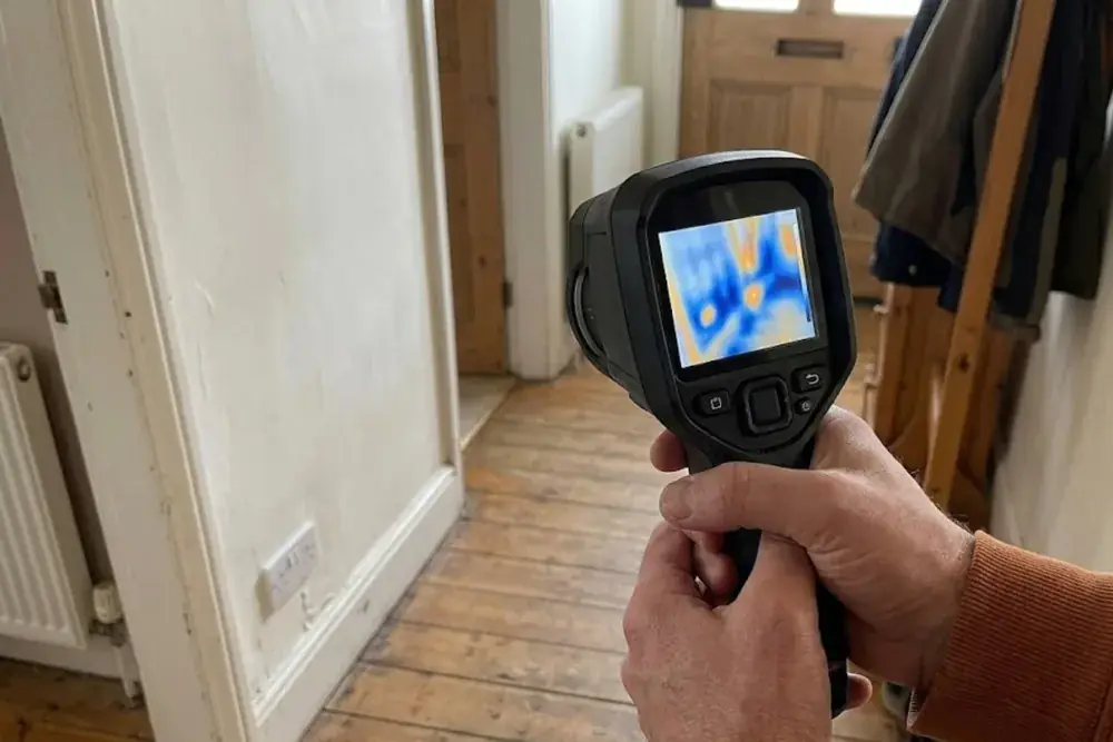 A hand holding a thermal imaging camera in a hallway to look for hidden moisture