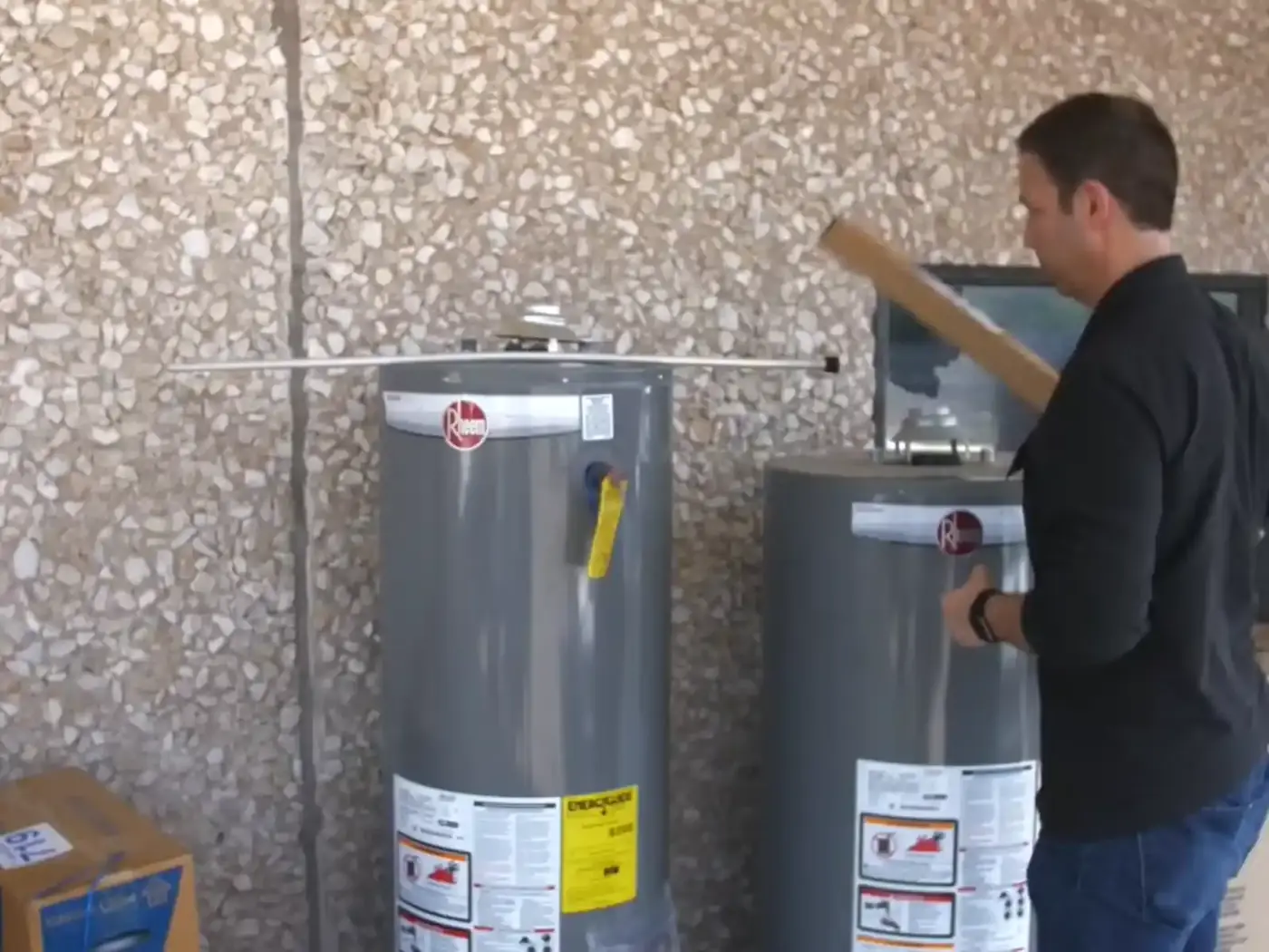 A technician standing between two new tank water heaters with cartons stacked behind them